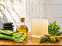 Olive oil, soap, and aloe vera on a wooden surface with a tiled wall background