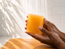 Hand holding a yellow bar of soap under running water in a shower.