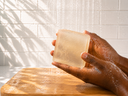 Hand holding a bar of soap under running water with a tiled wall background