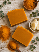 Two orange soap bars on a wooden surface with turmeric powder and butter.