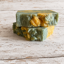 Two green and yellow marbled soap bars stacked on a wooden surface